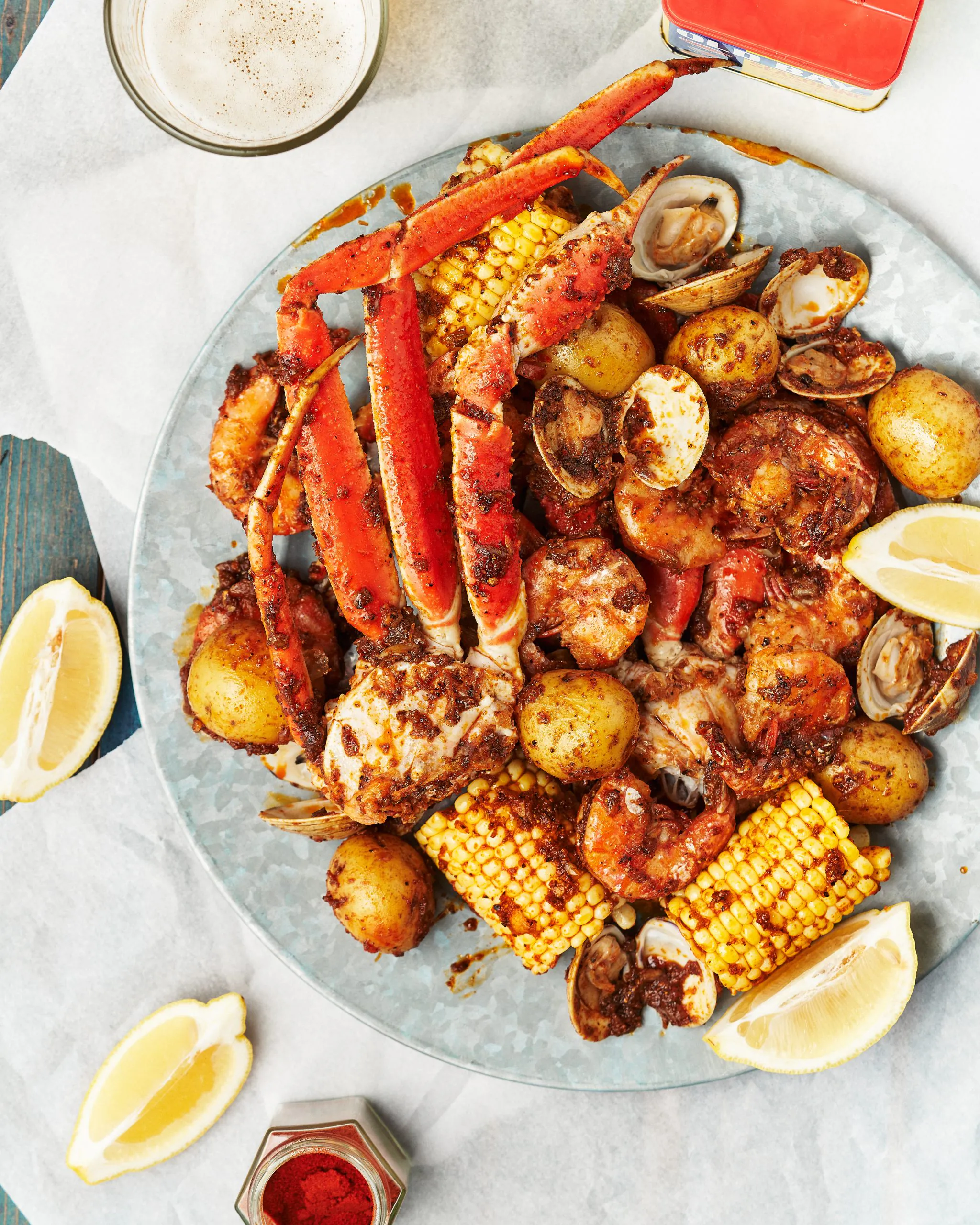 A seafood boil platter featuring seasoned crab legs, shrimp, clams, corn on the cob, and small potatoes, garnished with lemon wedges and Old Bay seasoning.